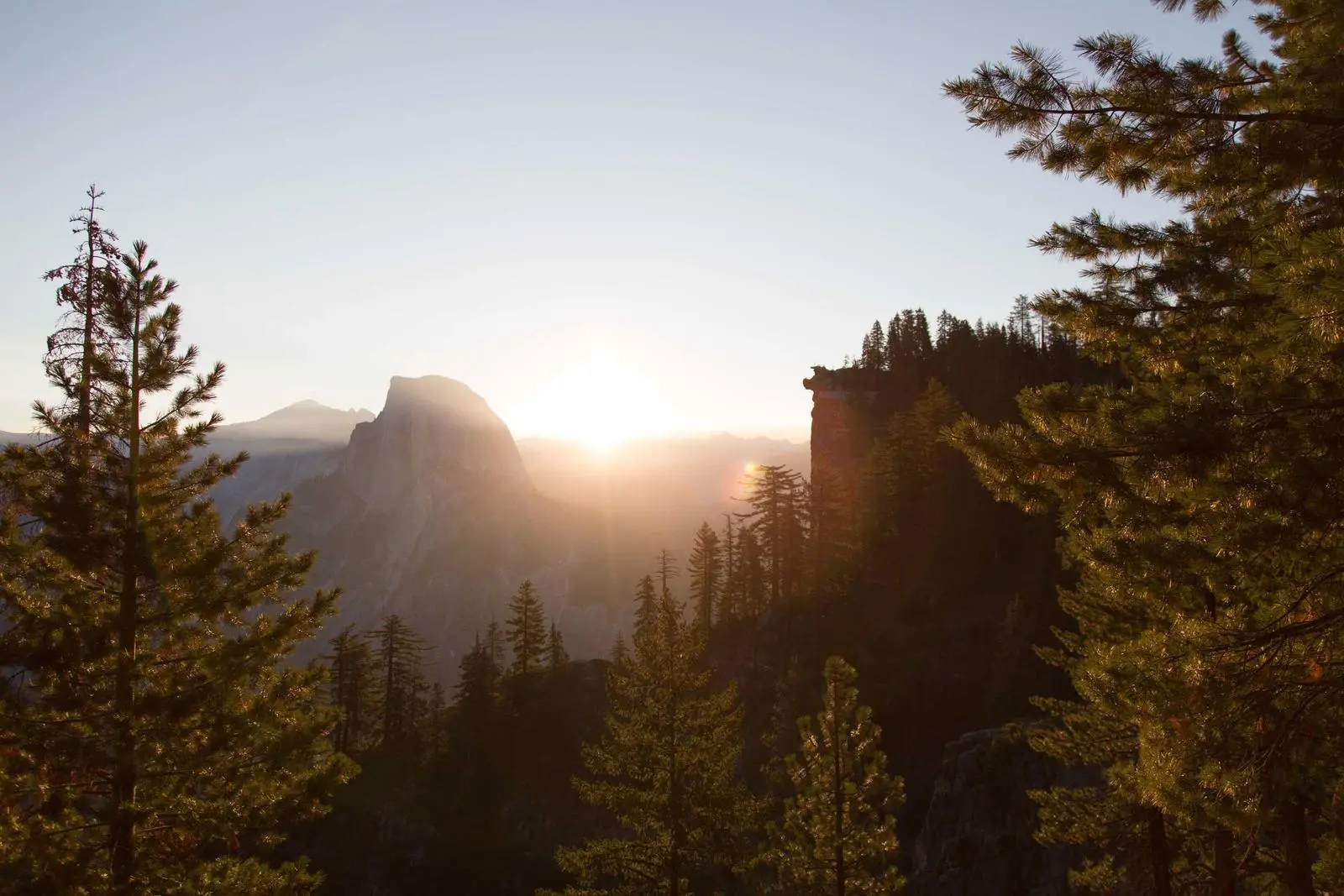 Sonnenaufgang, der durch Bäume in einem Bergtal bricht