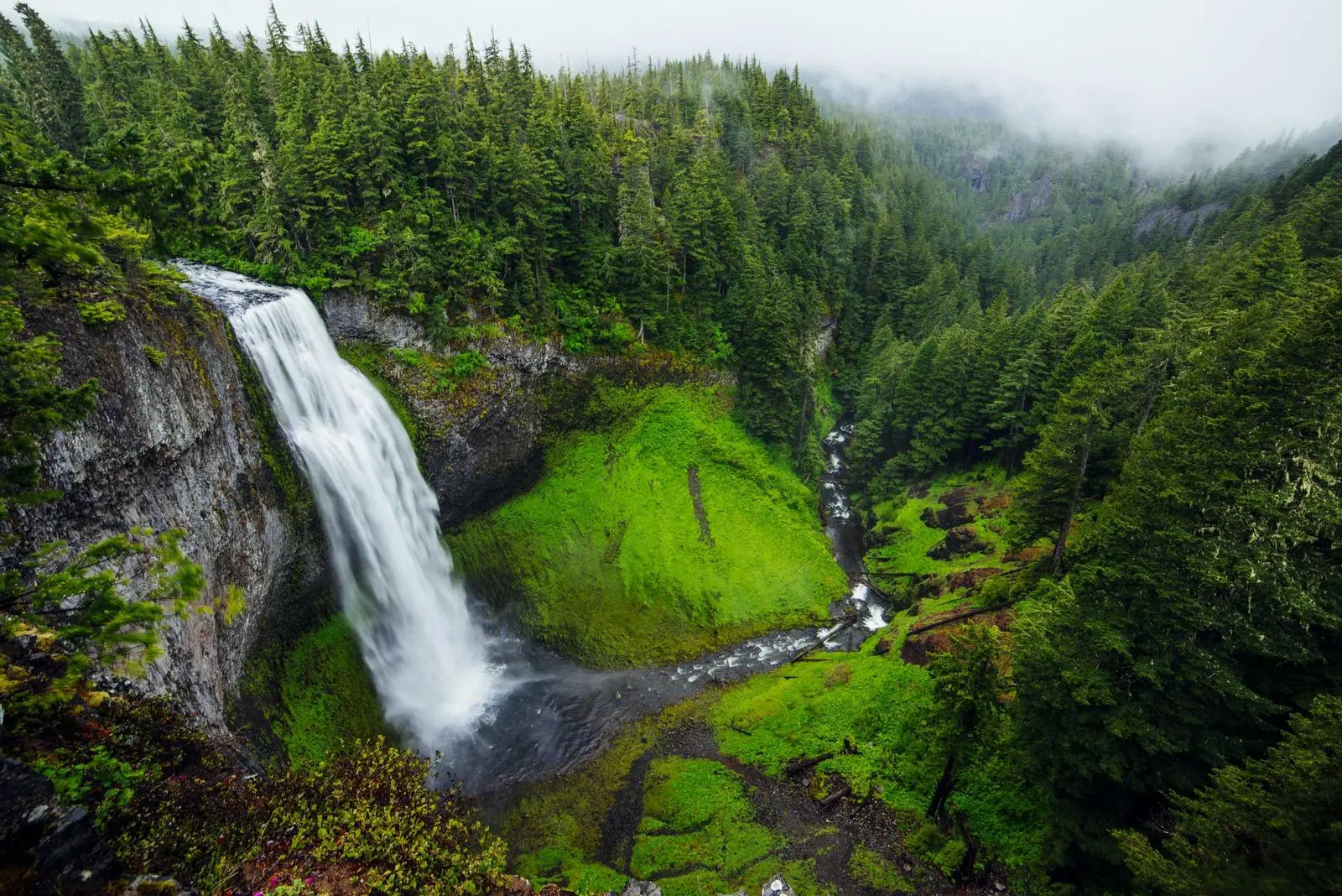 Wasserfall fließt in ein grünes, nebliges Tal